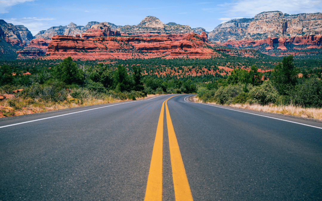 Open highway leading to red rock formations under a clear blue sky in Sedona, Arizona