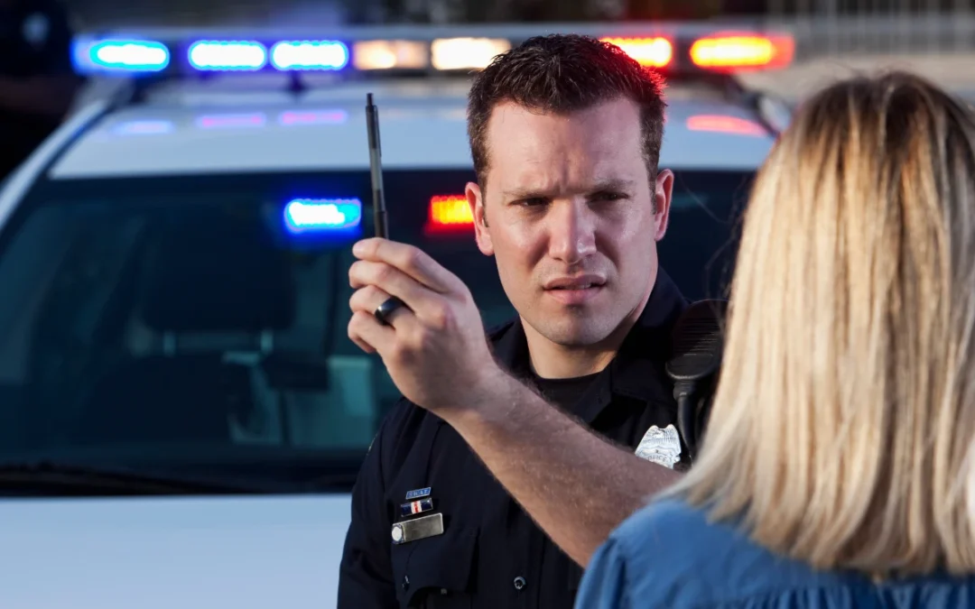 A police officer holding a pen, conducting a DUI screening with a driver pulled over at the roadside, highlighting the initial step in identifying potential alcohol misuse.