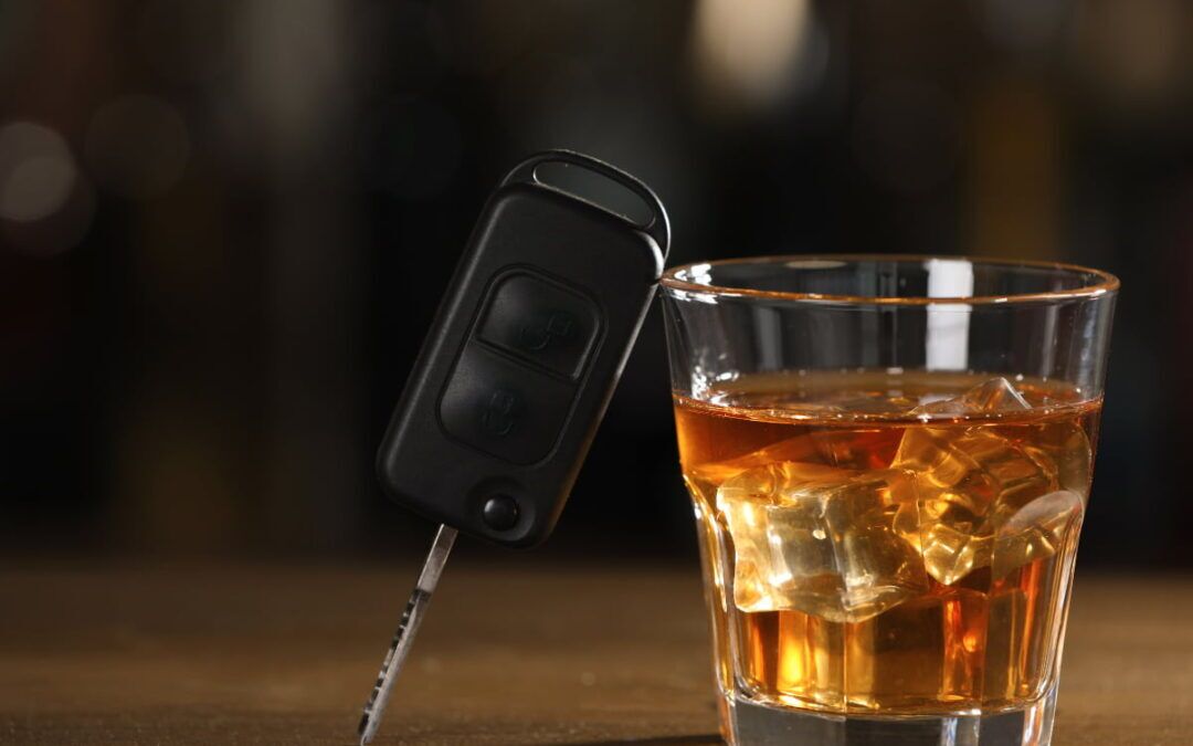 A car key leaning on a glass of alcohol.