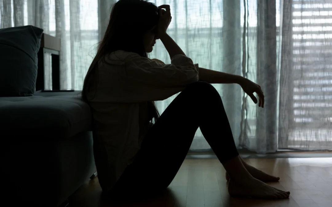 A distressed woman sitting on the edge of his bed in a dimly lit room, holding his head in his hands, symbolizing the emotional toll of a DUI charge and its impact on mental health.