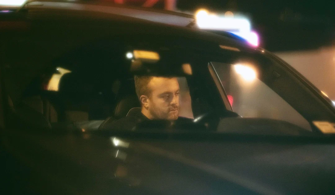 A man looking at his side mirror as the traffic officers tail him in the foreground.